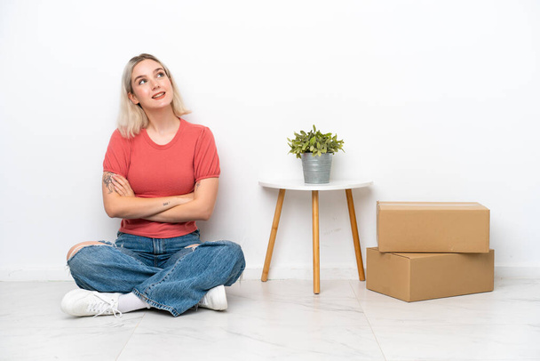 Молода жінка рухається в новому будинку серед коробки ізольовані на білому тлі, дивлячись вгору, коли посміхається
 - Фото, зображення