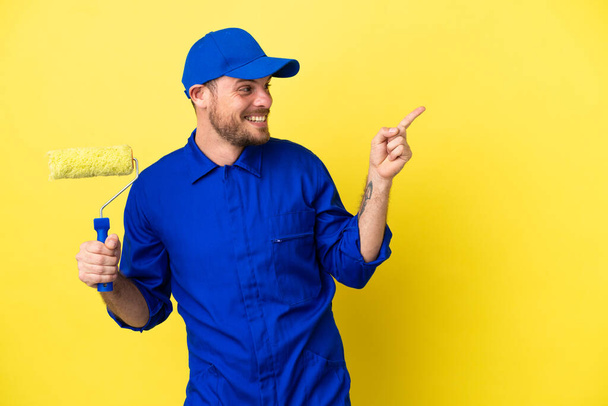 Maler brasilianischer Mann isoliert auf gelbem Hintergrund zeigt mit dem Finger zur Seite und präsentiert ein Produkt - Foto, Bild