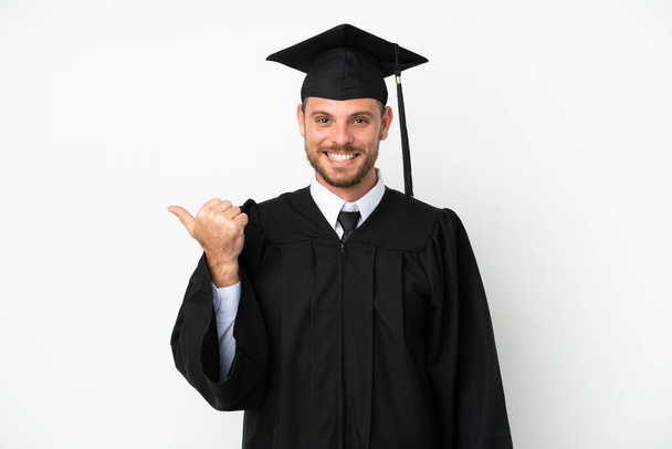 Молодой выпускник бразильского университета изолирован на белом фоне, указывая в сторону, чтобы представить продукт - Фото, изображение