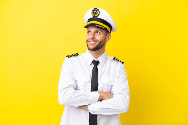 Airplane caucasian pilot isolated on yellow background looking up while smiling - Photo, Image