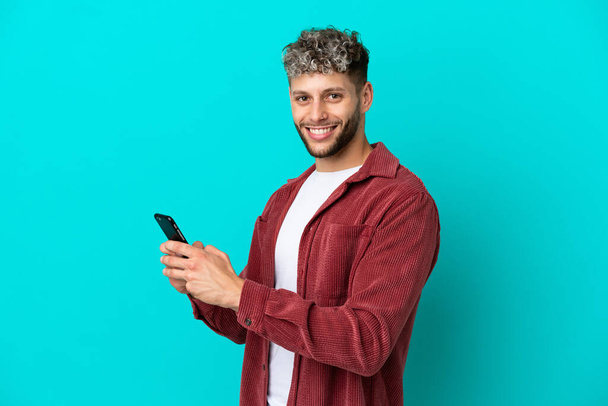 Young handsome caucasian man isolated on blue background sending a message or email with the mobile - Фото, зображення