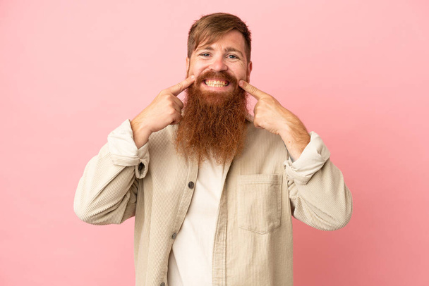 Young reddish caucasian man isolated on pink background smiling with a happy and pleasant expression - Foto, afbeelding