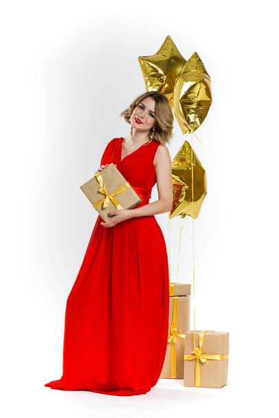 Party photo of elegance sexy lady in red dress with red lips and blond beautiful curly hair, smiling. Background of gold air balloons and gifts. Concept of the sale - Foto, immagini