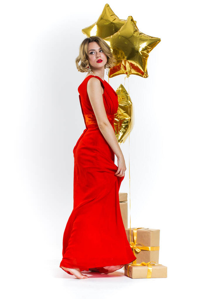 Partyfoto von Eleganz sexy Dame in rotem Kleid mit roten Lippen und blonden schönen lockigen Haaren, lächelnd. Hintergrund der goldenen Luftballons und Geschenke. Konzept des Verkaufs - Foto, Bild