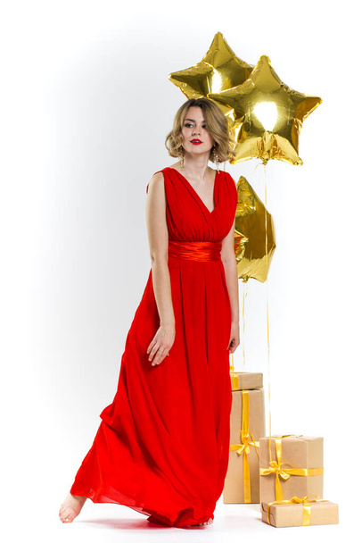 Party photo of elegance sexy lady in red dress with red lips and blond beautiful curly hair, smiling. Background of gold air balloons and gifts. Concept of the sale - Foto, Imagen