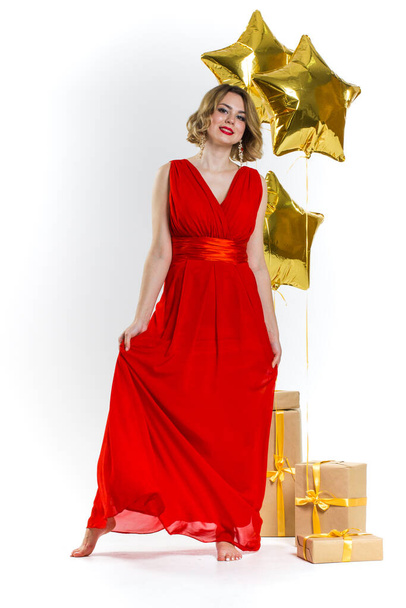 Party photo of elegance sexy lady in red dress with red lips and blond beautiful curly hair, smiling. Background of gold air balloons and gifts. Concept of the sale - Fotoğraf, Görsel