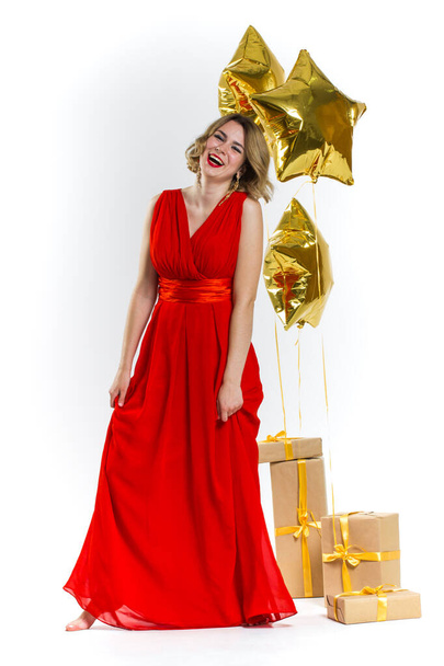Party photo of elegance sexy lady in red dress with red lips and blond beautiful curly hair, smiling. Background of gold air balloons and gifts. Concept of the sale - Фото, зображення