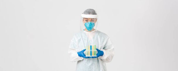 Ковид-19, коронавирусная болезнь, концепция медицинских работников. Удивлённая азиатская женщина-врач, техническая лаборатория в персональном защитном оборудовании, проведение пробирки с вакциной или анализами, белый фон - Фото, изображение