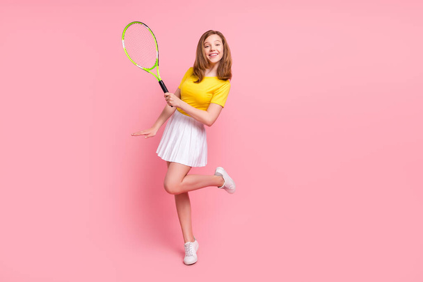 Full body photo of nice blond teen girl play tennis wear yellow t-shirt skirt isolated on pink color background - 写真・画像