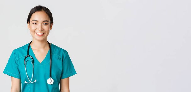 Healthcare workers, preventing virus, quarantine campaign concept. Close-up of smiling pleasant asian female nurse, physician in scrubs looking upbeat, listening to patient, white background - Photo, Image