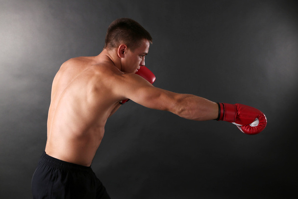 Handsome young muscular sportsman with boxing gloves on dark background - Foto, Bild