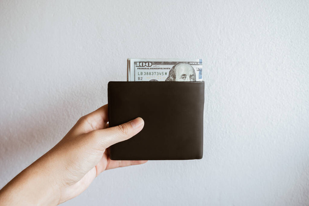 Przycięte zdjęcie kogoś trzymającego skórzany portfel z amerykańską walutą banknotów (100 dolarów) w środku. Dolar amerykański jest walutą amerykańską, jak również światową walutą rezerwową. - Zdjęcie, obraz