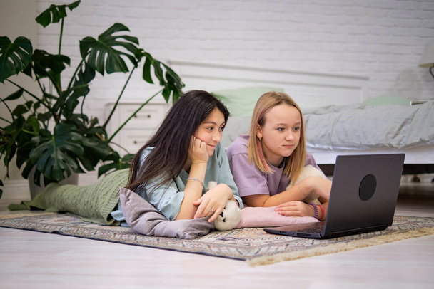 dvě dospívající dívky leží na podlaze ložnice a dívají se na film na notebooku. Koncept přátelství - Fotografie, Obrázek