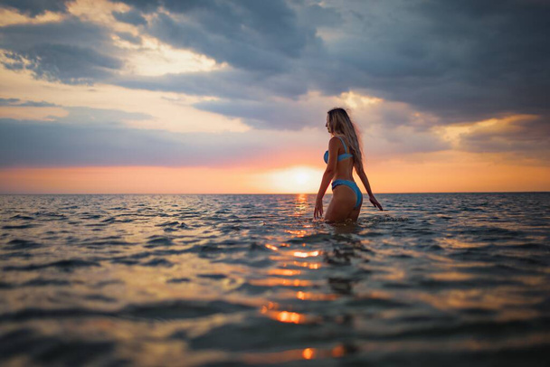 Girl with blond hair in a swimsuit posing against the backdrop of the sunset in the estuary enjoying nature around him - Foto, afbeelding