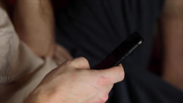 male hands with a smartphone close-up. A man sits in a chair resting and using a mobile phone, swiping, turning pages, choosing and shopping online. Searching for information on the Internet - Footage, Video