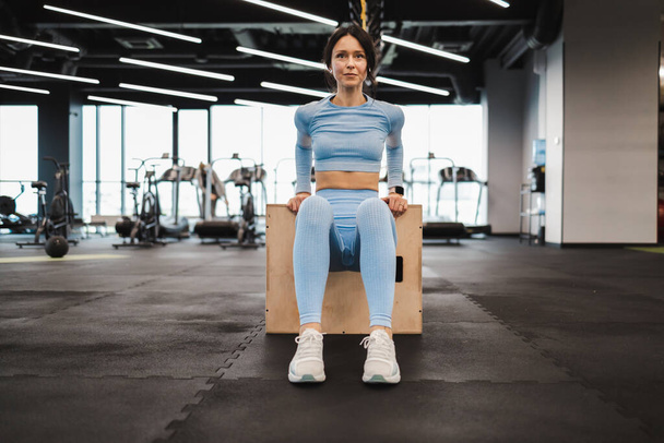 Donna atletica in abbigliamento sportivo blu che fa esercizi tricipiti su scatola di salto in legno crossfit in palestra - Foto, immagini