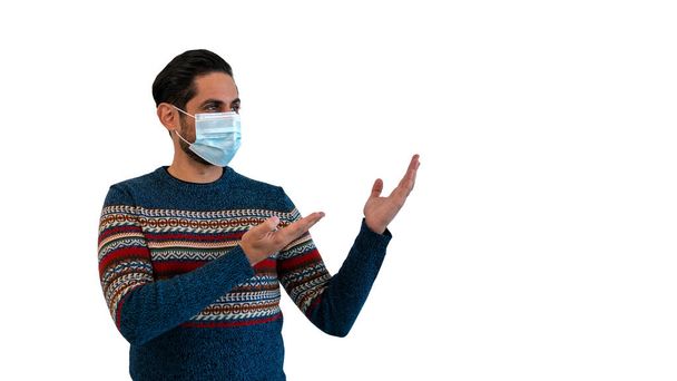 Caucasian man pointing with two hands to the side with medical mask during corona virus outbreak. Person looking to copy space aside for promotional text or advertisement on white studio background - Photo, Image