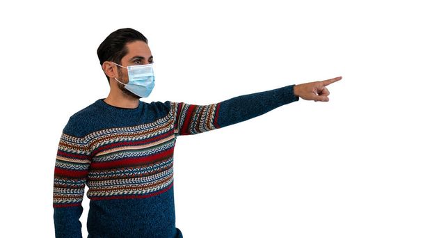 Man indicates with a finger to the side and using face mask safe from coronavirus. Person looking to copy space aside for promotional text or advertisement on white studio background. - Фото, зображення