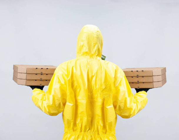 a food deliveryman in a yellow suit and a protective gas mask - Фото, изображение