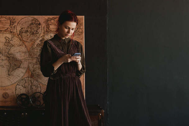 Mladá žena stojící na obraze v moderním bytě drží mobilní telefon - Fotografie, Obrázek