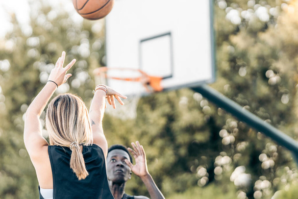 Selective focus on a woman shooting a ball at the basket while a man defends it - Photo, Image
