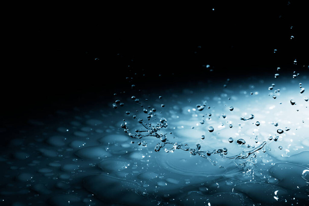 Beautiful splash blue background a drop of water crashed on a hard surface. In blue light on a black - Foto, imagen