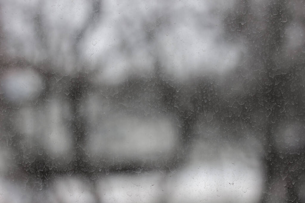 Szkło pokryte suchymi kroplami deszczu. Śnieg pada przez okno w chłodny zimowy dzień. - Zdjęcie, obraz