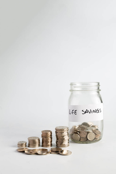 Concepto de ahorro de dinero y valor creciente con el tiempo, pilas de monedas de plata que se componen y crecen junto a un frasco con monedas en ahorros etiquetados de por vida - Foto, Imagen