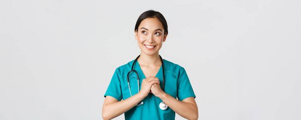 Healthcare workers, preventing virus, quarantine campaign concept. Determined and confident asian female physician in scrubs, clench hands together, getting ready, looking upper left corner - Photo, image