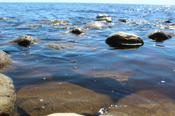 agua clara que fluye sobre piedras grandes en verano / piedras de fotos y agua. piedras grandes yacen en el agua. hay agua clara entre las piedras. los reflejos del sol se reflejan en el agua. hermoso paisaje. - Foto, Imagen