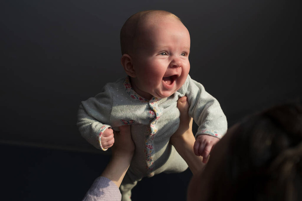 Жінка торкається чола зі своєю новонародженою дитиною, піднімаючи його проти вікна вдома
 - Фото, зображення