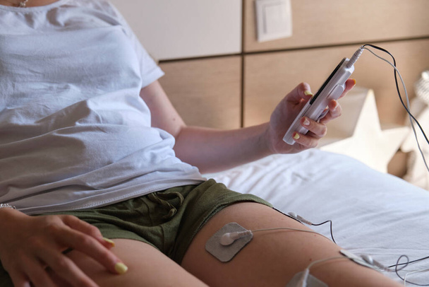 electrostimulation treatment at home, electrodes on the leg of an unrecognizable woman, getting a treatment of tens, ems or massages to improve muscle health and improve blood circulation. injury recovery - Photo, Image