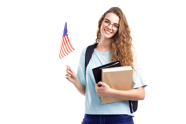 Smiling student girl in glasses with backpack holds books, notebooks and flag USA on white background - Photo, Image
