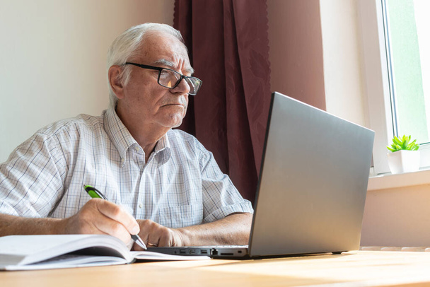 головна тема не зосереджена, старший старий чоловік сидить поруч за столом, домашній офіс онлайн ноутбук робота бізнес-відстань фрілансер
 - Фото, зображення