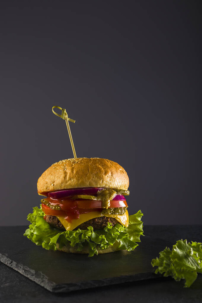 Leckeres Fast Food. Frischer saftiger Burger auf schwarzem Hintergrund auf einer Schiefertafel. Vertikale Position. Kopierraum - Foto, Bild