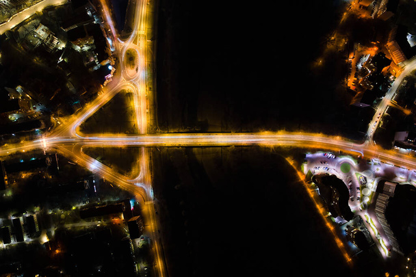 Gece yoğun trafikte hızla ilerleyen kavşağın hava görüntüsü. Şehir ulaşımının en üst görüntüsü. Trafiğin yoğun olduğu saatte araç ışıkları bulanıklaşıyor. - Fotoğraf, Görsel