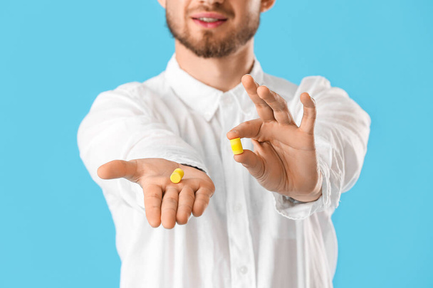 Young man with ear plugs on blue background, closeup - Foto, Imagen