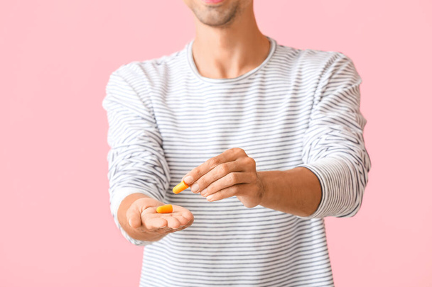 Young man with yellow ear plugs on pink background - Foto, imagen