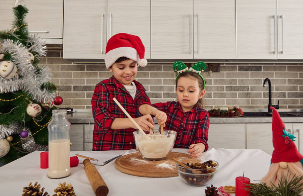 Handsome Caucasian children, beautiful preschooler girl and handsome school boy, loving brother and sister preparing Christmas cake dough together in the home kitchen. Happy relationships concept - Fotó, kép