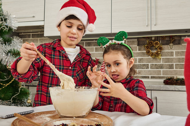 Adoráveis crianças europeias se divertindo juntos, preparando massa para biscoitos de Natal, pão de gengibre, muffins na cozinha da casa. Irmão em Santa chapéu e sua irmã mais nova em aro de elfo amassar massa - Foto, Imagem