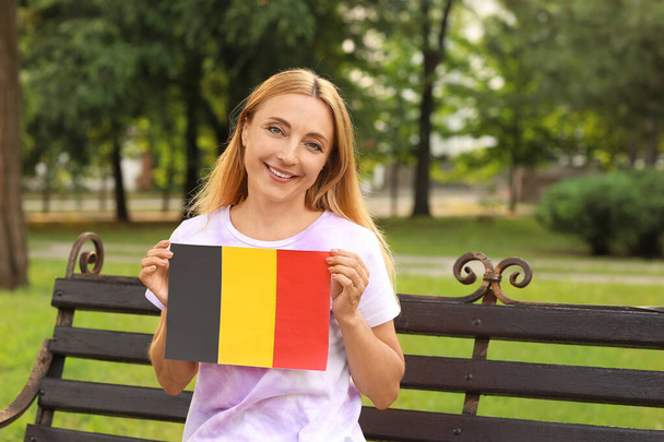 Dojrzała kobieta z flagą Belgii siedzi na ławce w parku - Zdjęcie, obraz