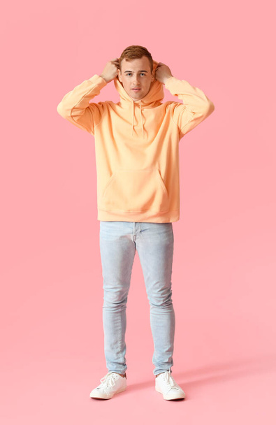 Junger Kerl in stylischem Kapuzenpulli auf farbigem Hintergrund - Foto, Bild