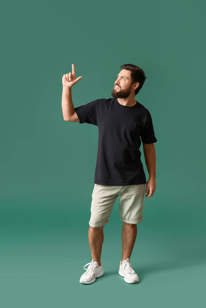 Handsome man in black t-shirt pointing at something on green background - Фото, зображення