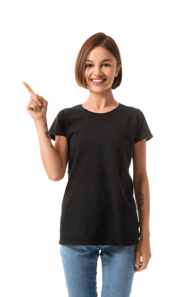 Beautiful young woman in stylish t-shirt pointing at something on white background - Photo, Image