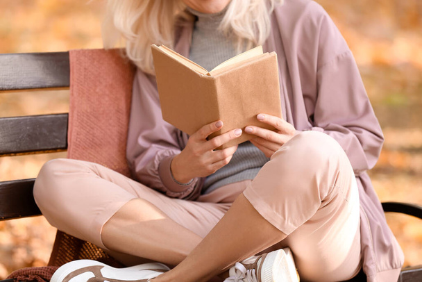 Sonbahar parkında kitap okuyan olgun bir kadın. - Fotoğraf, Görsel