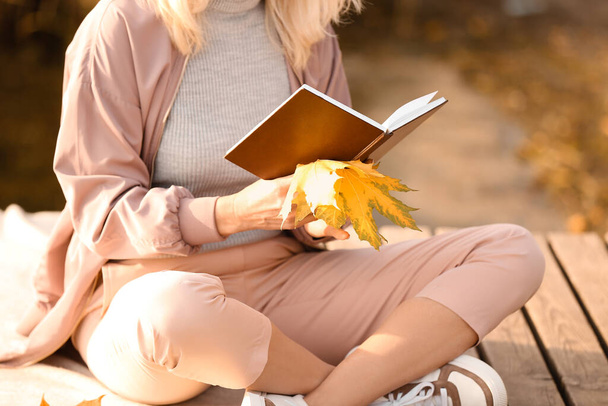 Mature woman reading book near river on autumn day - 写真・画像