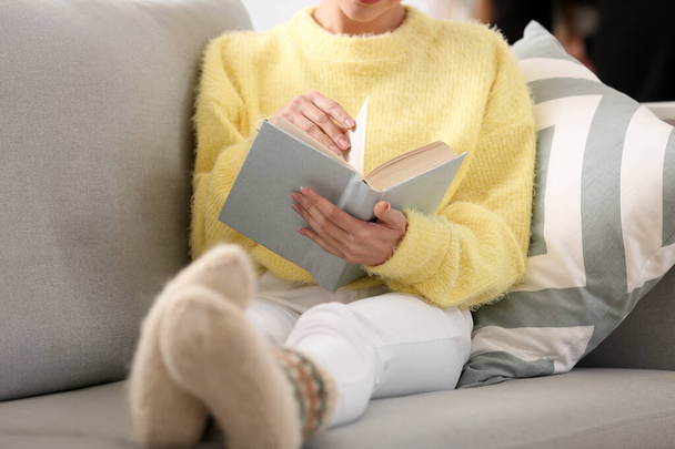 Young woman reading book on sofa at home, closeup - Фото, изображение