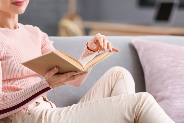 Young woman reading book on sofa at home, closeup - Photo, Image
