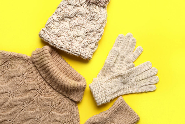 Warm hat, gloves and sweater on yellow background, closeup - Foto, imagen