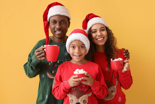 サンタの帽子のアフリカ系アメリカ人の家族と色の背景においしいホットチョコレートのカップ - 写真・画像